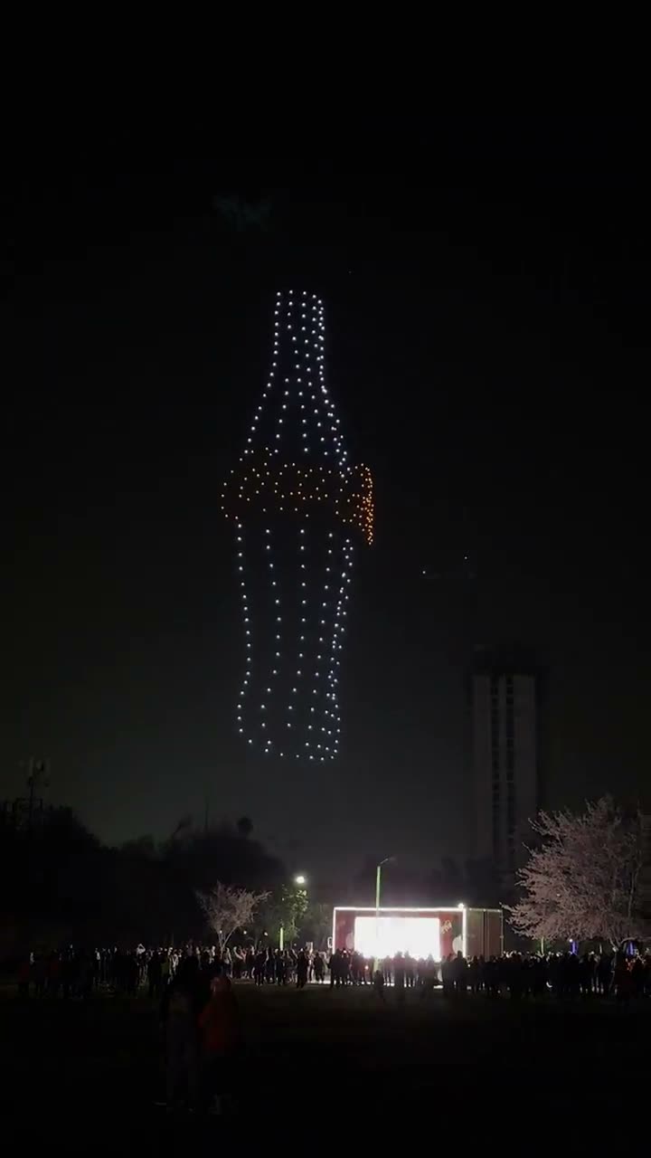 Enjambre de drones formando el contorno de una botella de Coca-Cola sobre el público de un evento nocturno