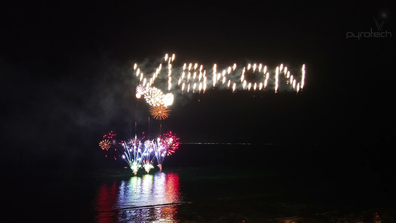 Drones y pirotecnia sobre el mar durante un evento en la playa al anochecer