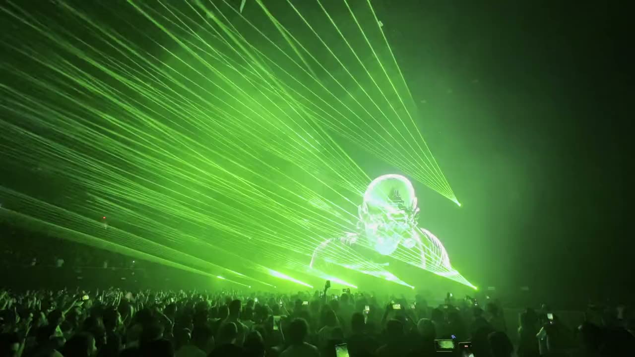 Green laser beams and a laser-drawn figure over a concert crowd